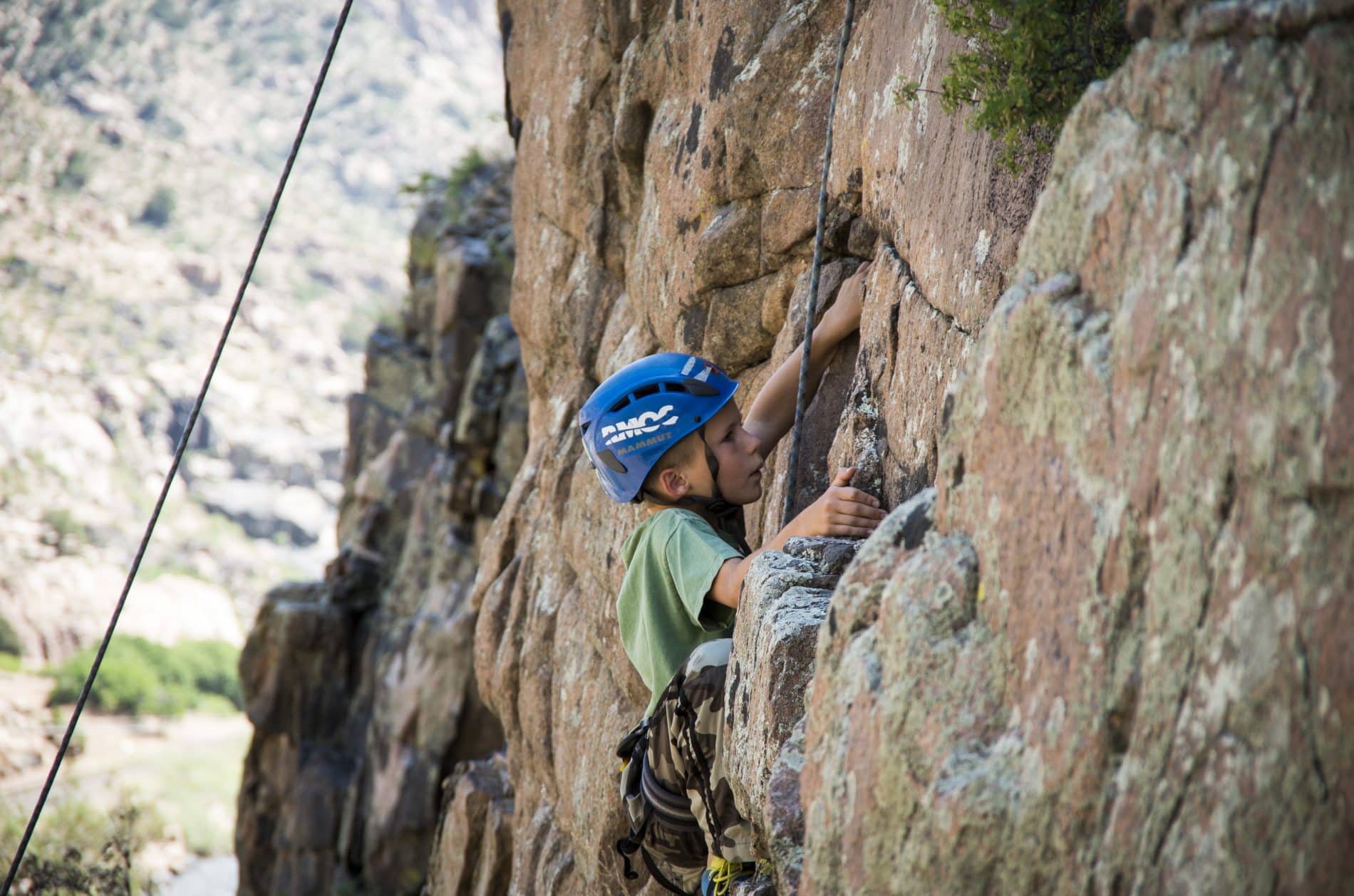 kid climbing a rock face with a helmet and ropes