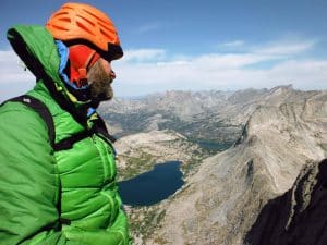 Climber in a bright green jacket at the top of a mountain